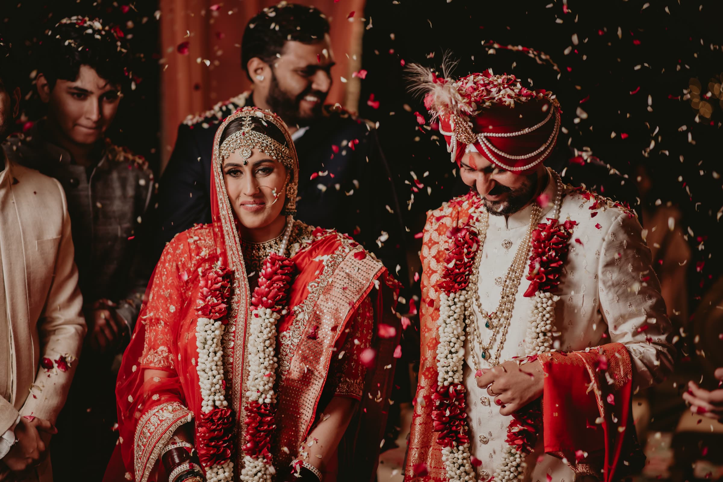 Couple in garlands beneath a shower of rose petals at the varmala