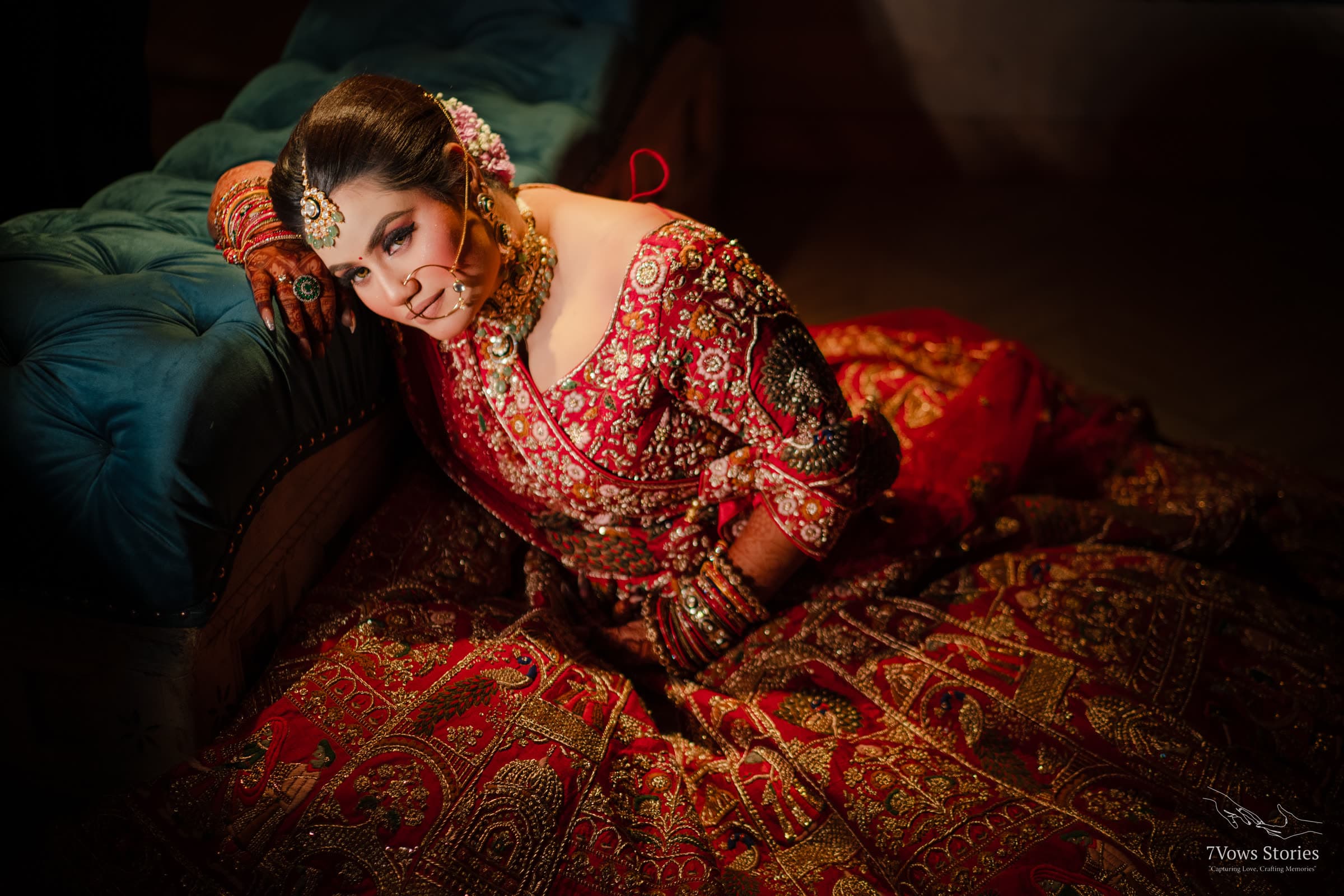 Bride in red bridal wear resting against a velvet sofa