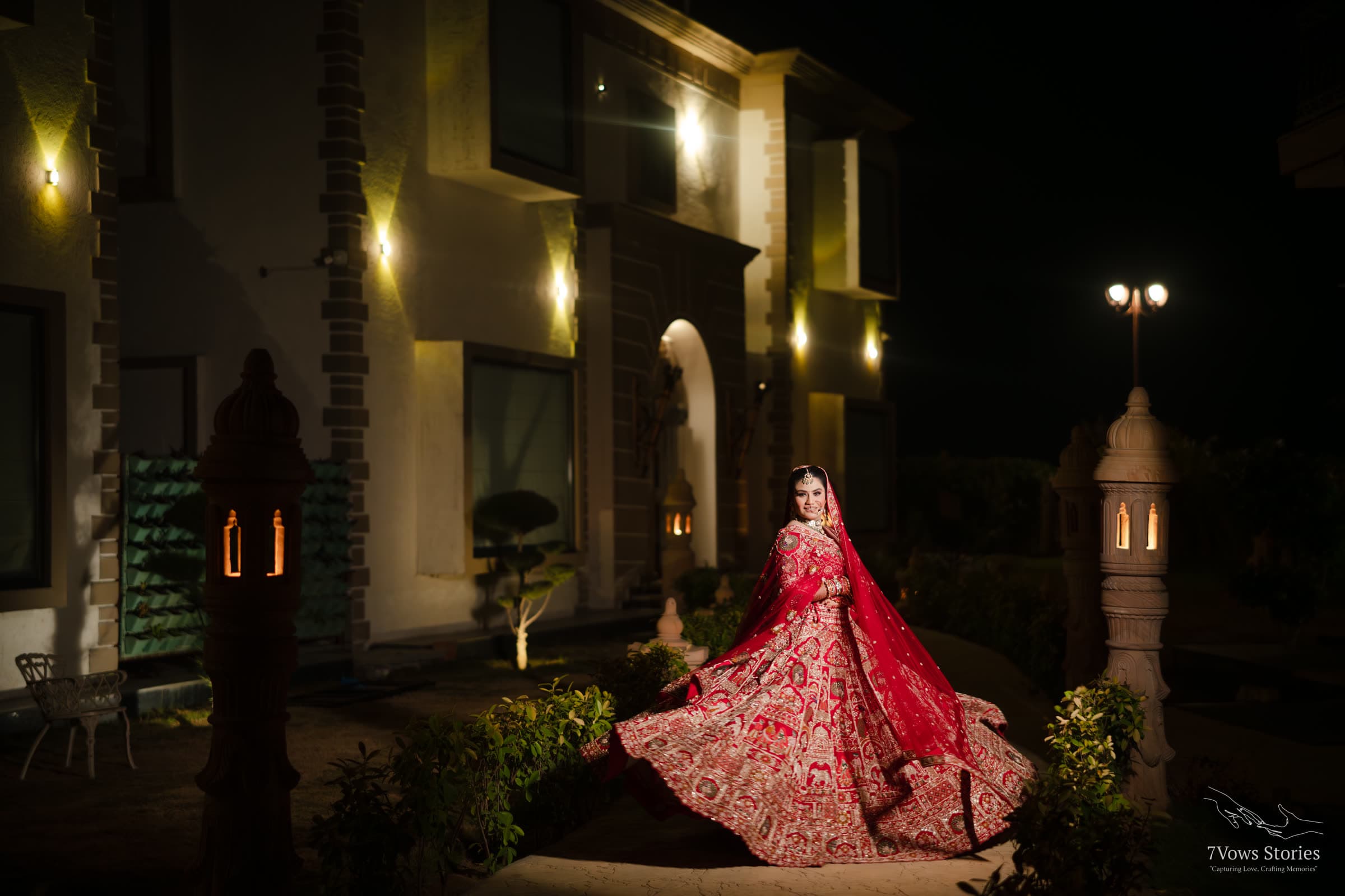 Bride twirling her red lehenga in a lantern-lit courtyard at night