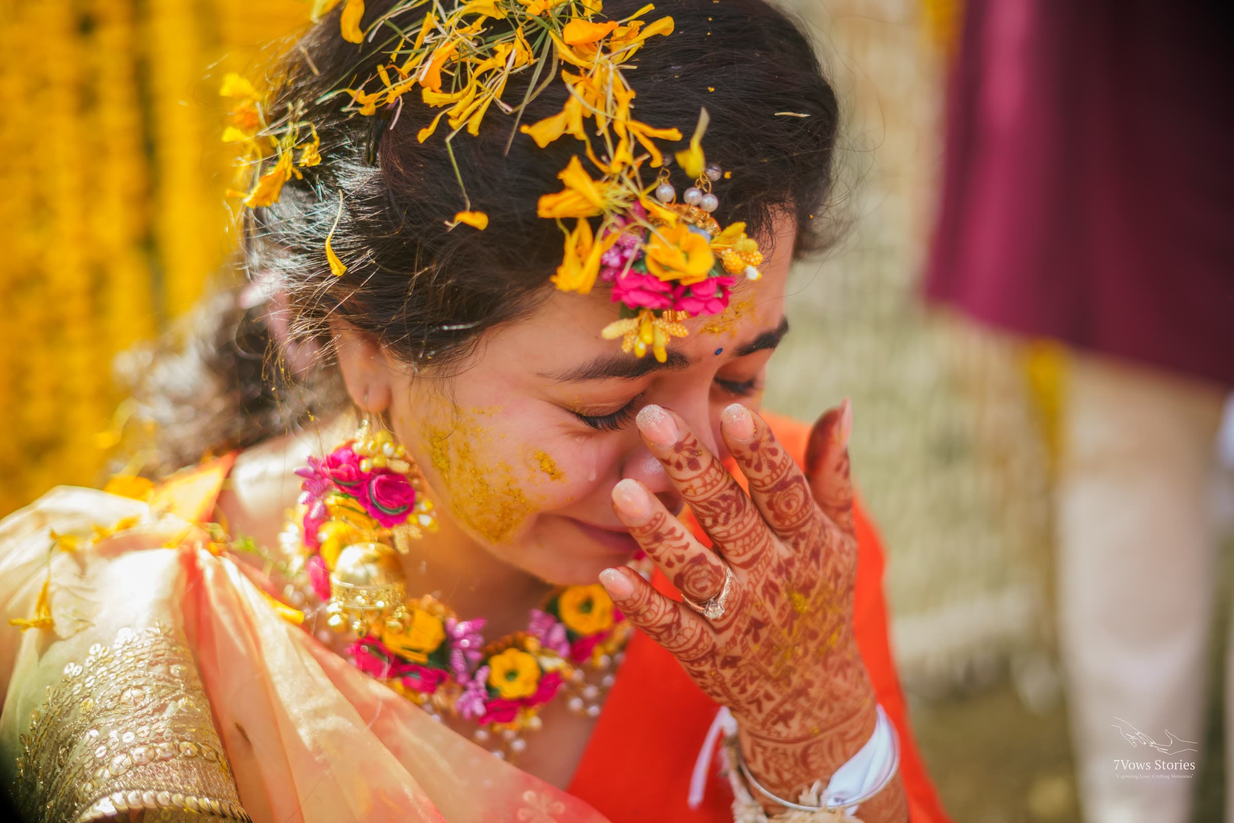 Bride wiping away a tear beneath falling marigold petals at her haldi